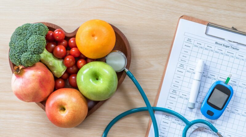 fruits in a heart-shaped dish and patient's blood sugar control record with diabetic measuring tool kit